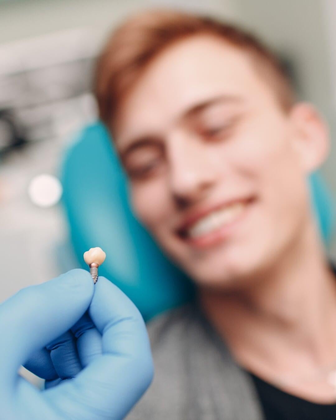 Man smiling while observing a dental implant with its crown.